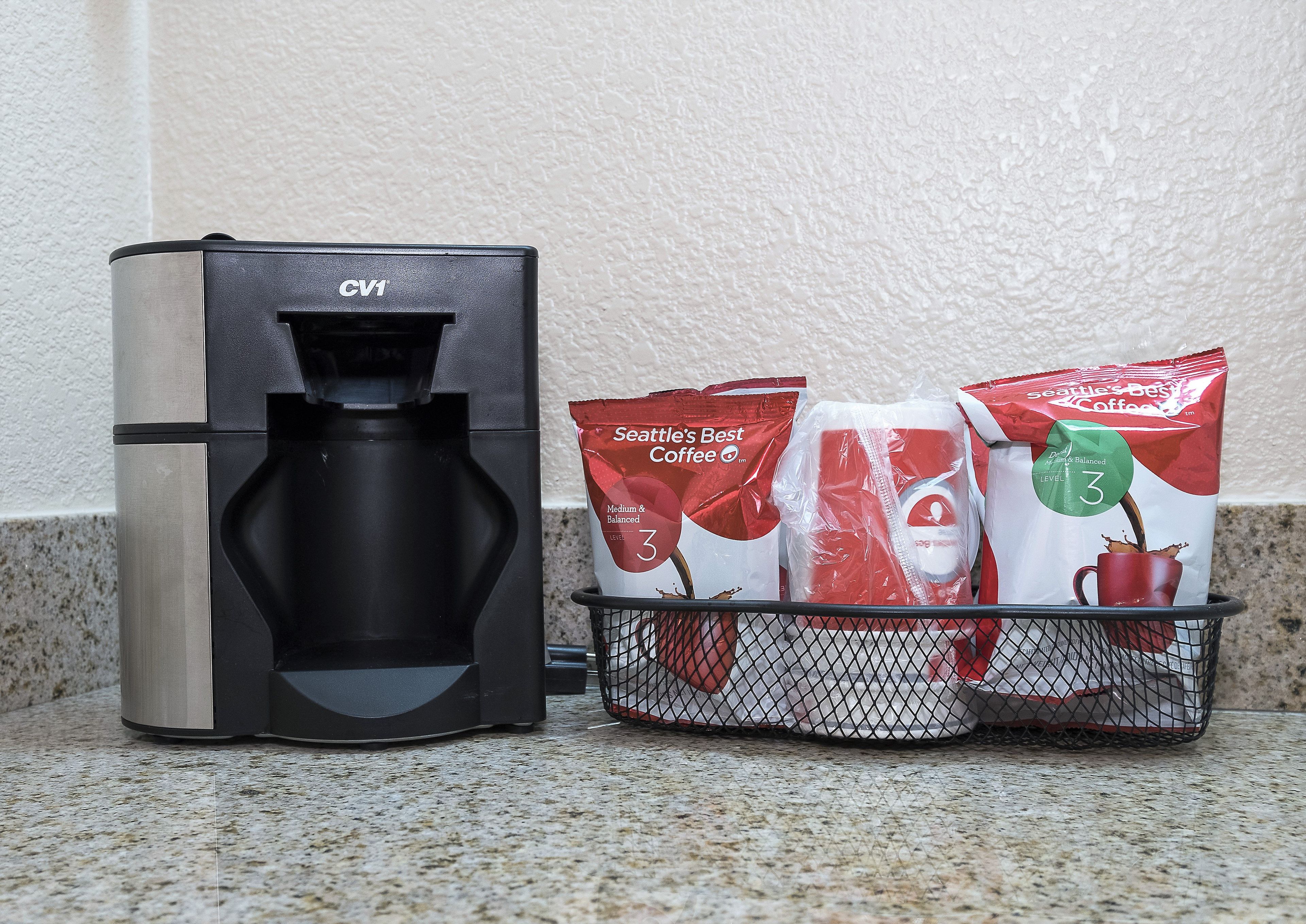 A coffee maker with a drip tray and a basket containing coffee pods and a reusable cup.