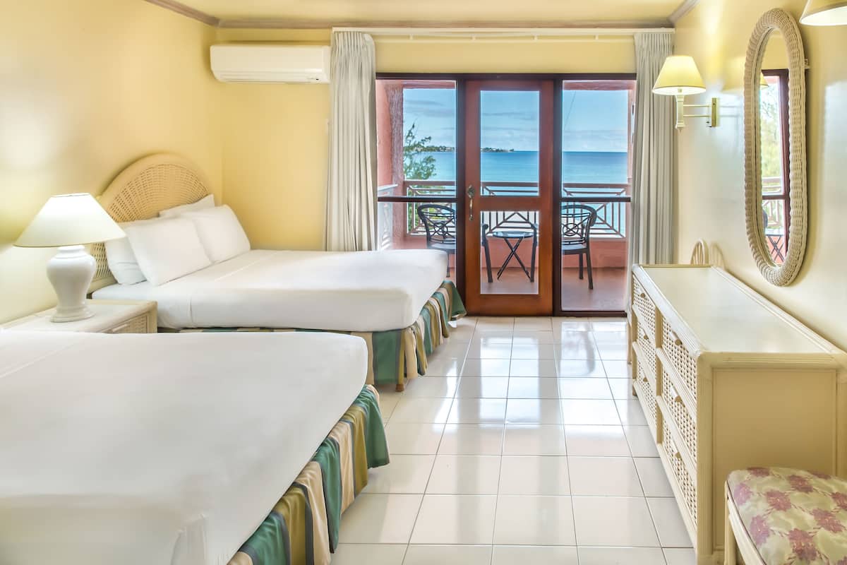 A hotel room with two beds, a balcony with a view of the sea, and a dresser.