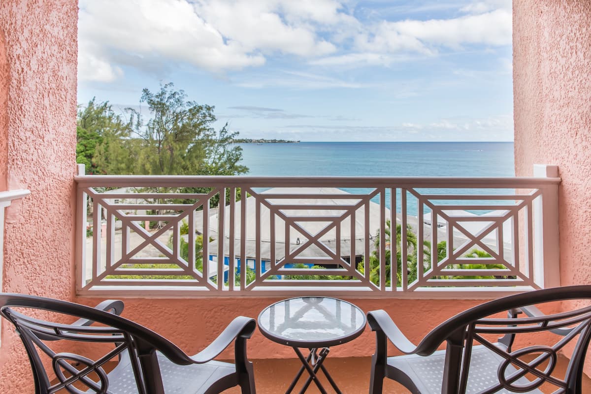 A balcony with a view of the sea, a table, and two chairs.