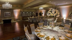 A banquet hall with round tables set for a formal event, featuring chandeliers, floral centerpieces, and a patterned wall.