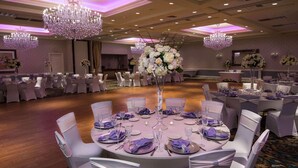 A banquet hall with round tables, white chairs, and purple table settings.