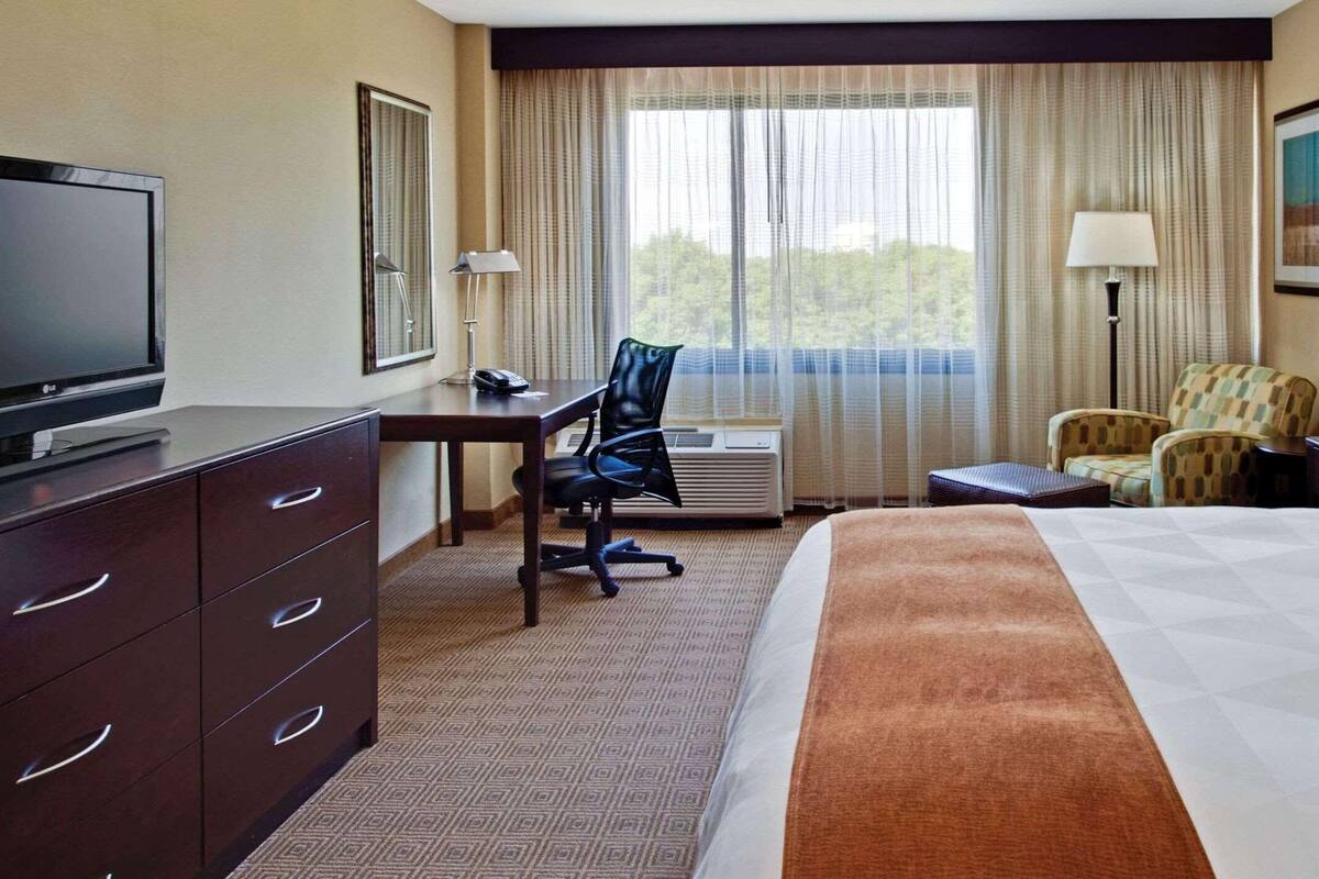 A hotel room with a bed, a desk with a chair, a television, and a window with curtains.