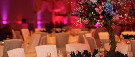 A banquet hall with round tables set for dining, each with a centerpiece of flowers and candles.