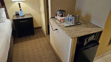 A hotel room with a bed, a nightstand with a lamp, a small kitchenette with a microwave, and a coffee maker.