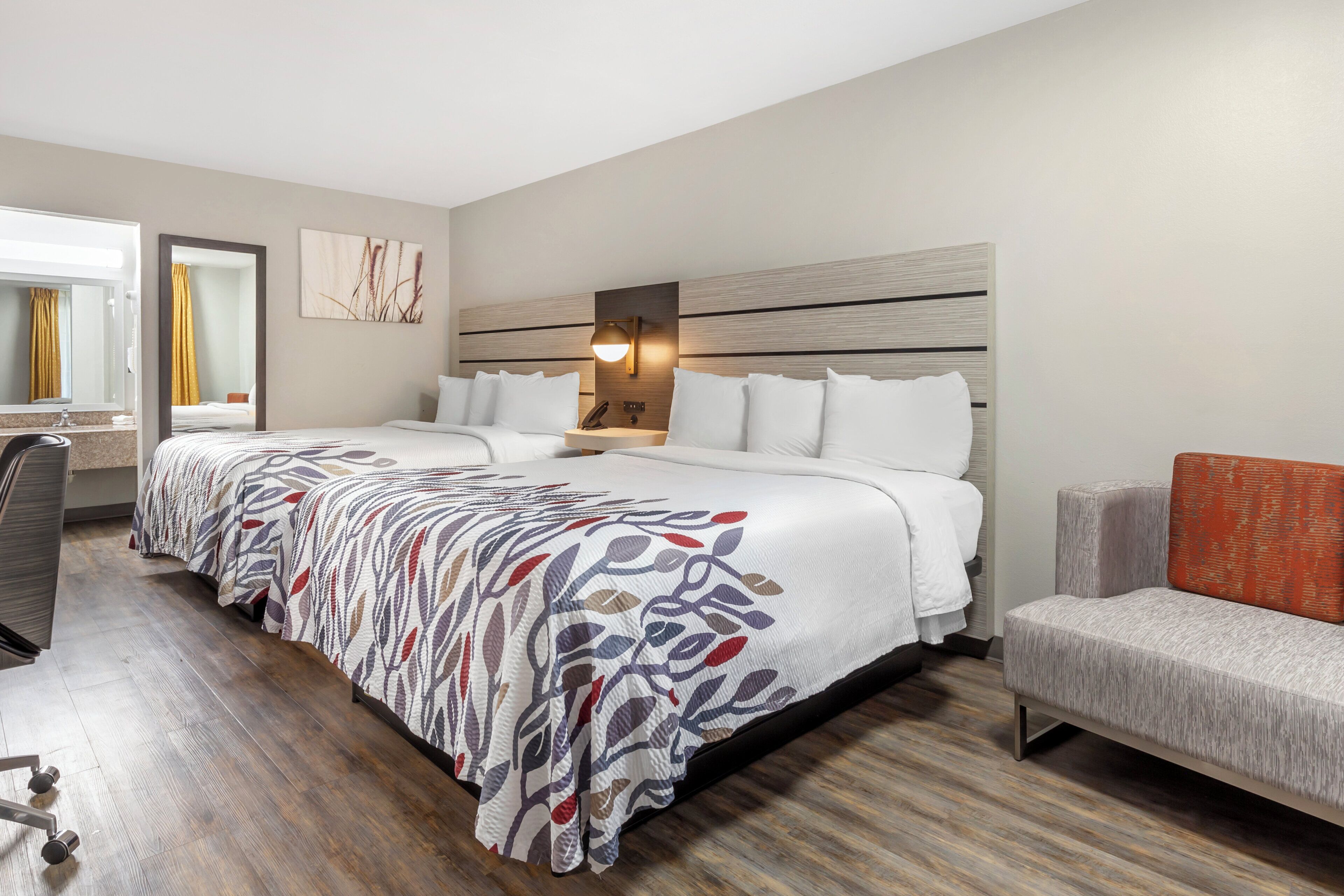 A hotel room with a large bed, a desk, a chair, and a nightstand.