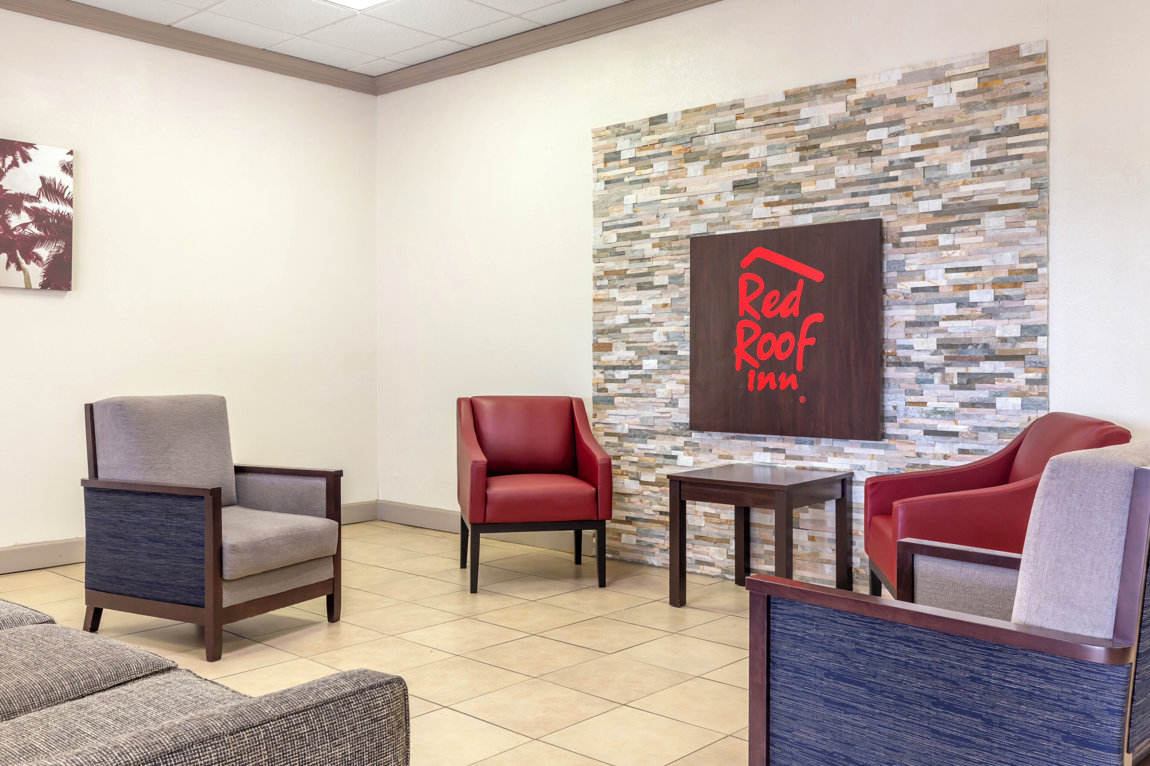 A lobby with a stone wall, a Red Roof Inn sign, and seating arrangements.