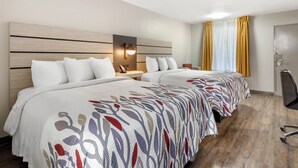 Habitación de hotel con dos camas, una mesita de noche, una lámpara, una silla y una puerta.