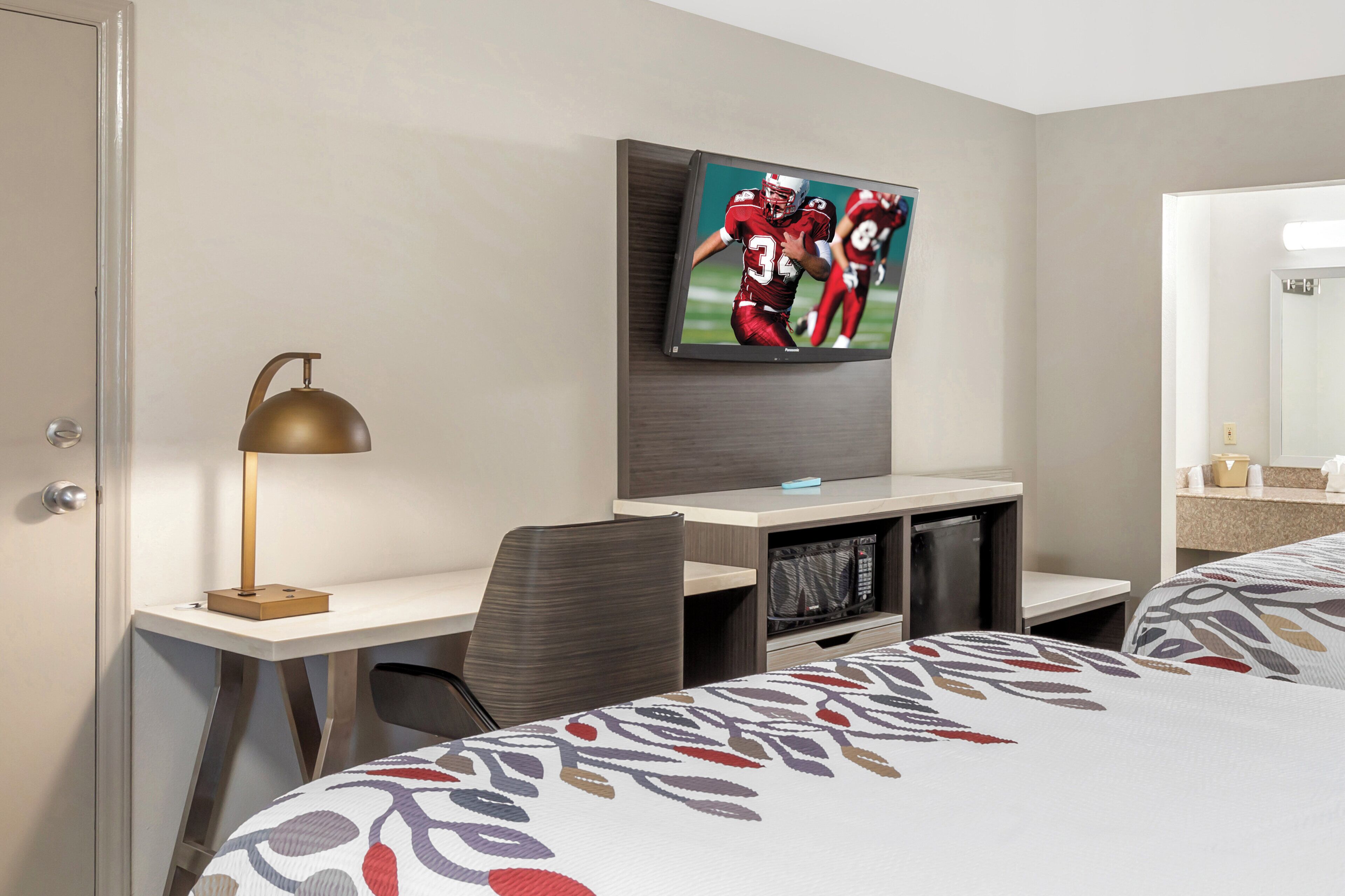 A hotel room with a bed, a desk, a television mounted on the wall, and a mirror.