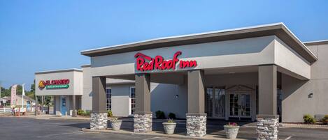 Un hotel Red Roof Inn con un diseño arquitectónico moderno, que cuenta con una entrada cubierta y un estacionamiento al frente.