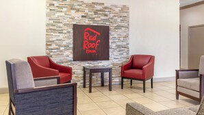 Vestíbulo de Red Roof Inn con pared de piedra, dos sillones de cuero rojo, una mesita y un sillón gris.