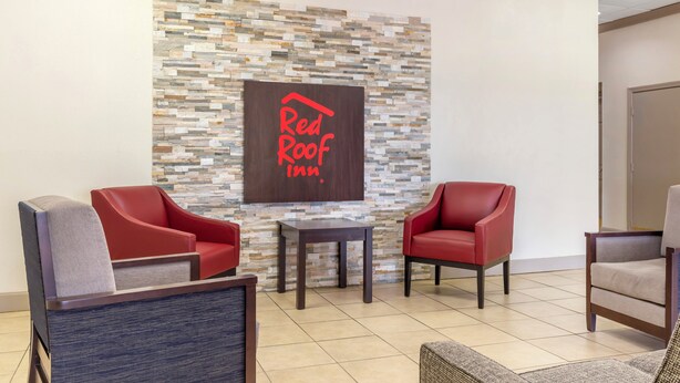 Vestíbulo de Red Roof Inn con pared de piedra, dos sillones de cuero rojo, una mesita y un sillón gris.