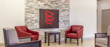 A Red Roof Inn lobby with a stone wall, two red leather armchairs, a small table, and a grey armchair.