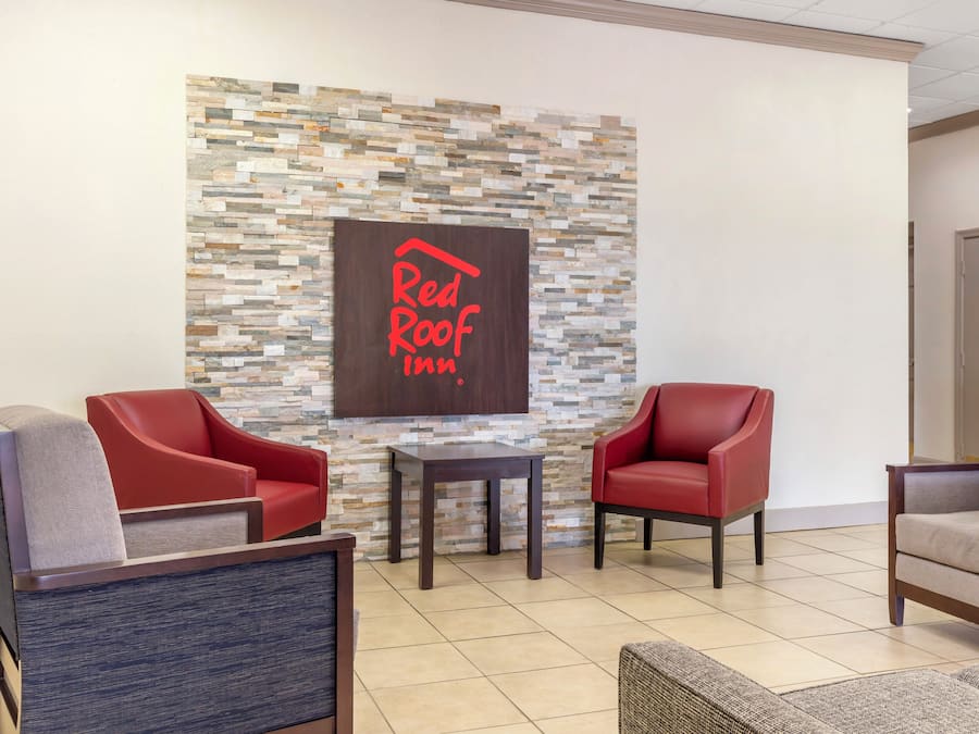 A Red Roof Inn lobby with a stone wall, two red leather armchairs, a small table, and a grey armchair.