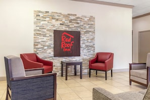 A Red Roof Inn lobby with a stone wall, two red leather armchairs, a small table, and a grey armchair. - Red Roof Inn Dunn (Dunn)
