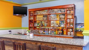Zona de bar con encimera de granito, varias botellas de licor, copas y un televisor montado en la pared.