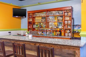 Zona de bar con encimera de granito, varias botellas de licor, copas y un televisor montado en la pared.