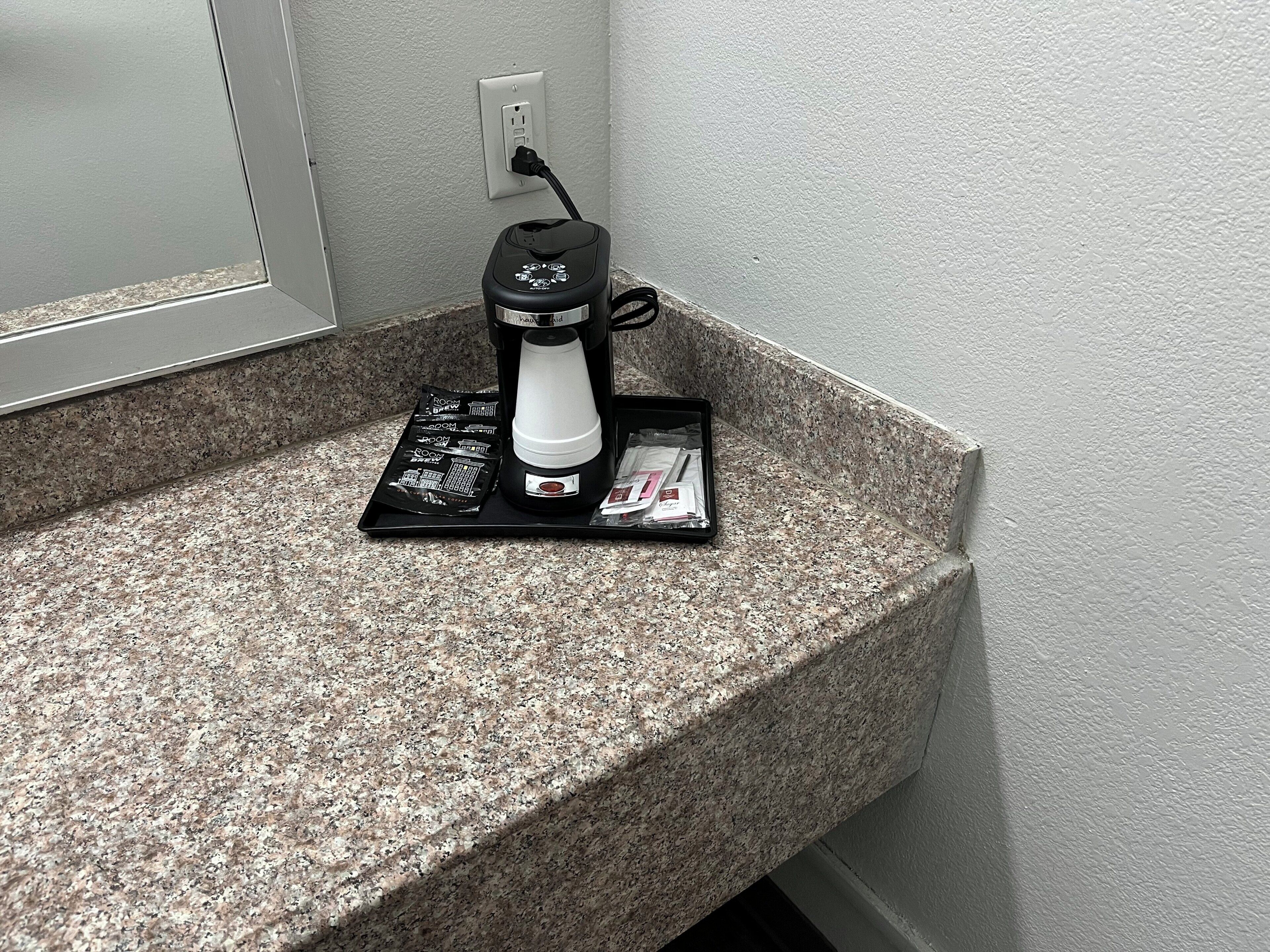 A coffee maker on a granite countertop with a power outlet in the background.