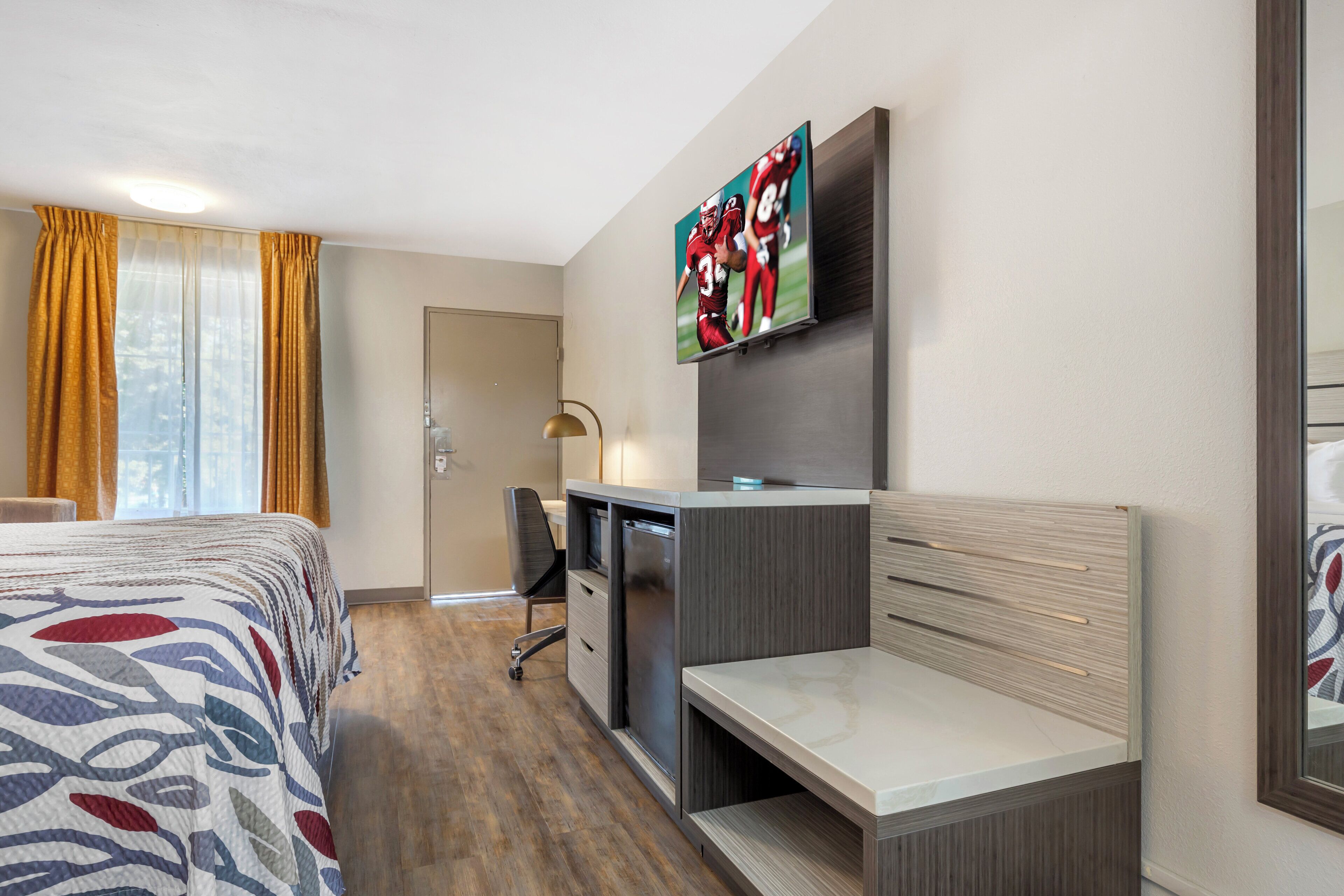 Une chambre d’hôtel équipée d’un lit, d’un bureau, d’une chaise et d’un téléviseur fixé au mur.