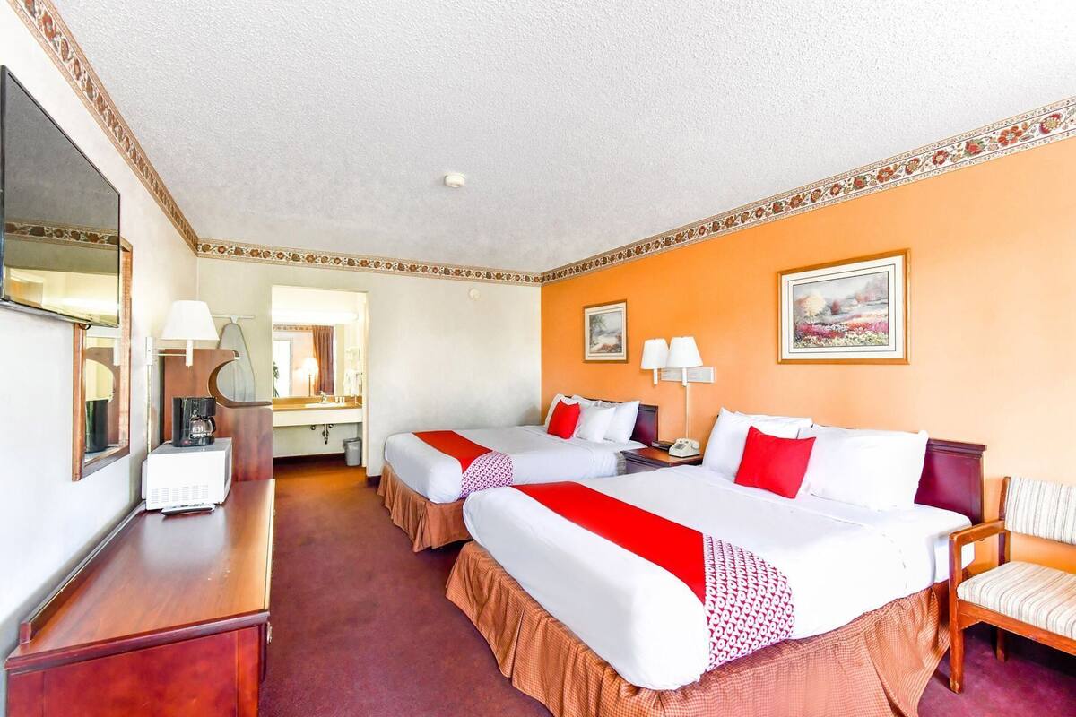Ein Hotelzimmer mit zwei Betten, einem Schreibtisch, einem Spiegel, einer Kaffeemaschine und einem Bild an der Wand.