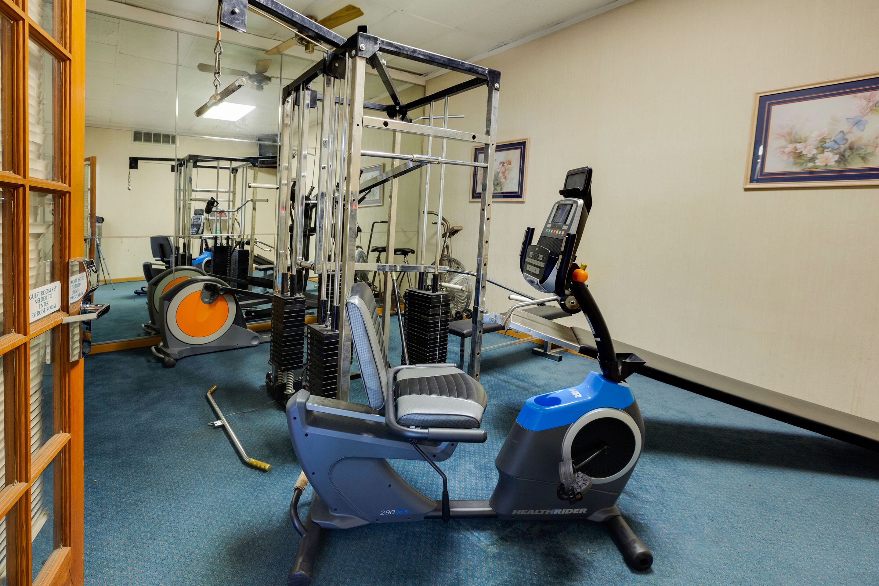 Uma academia com equipamentos de exercícios, incluindo bicicleta ergométrica, esteira e aparelho de musculação.