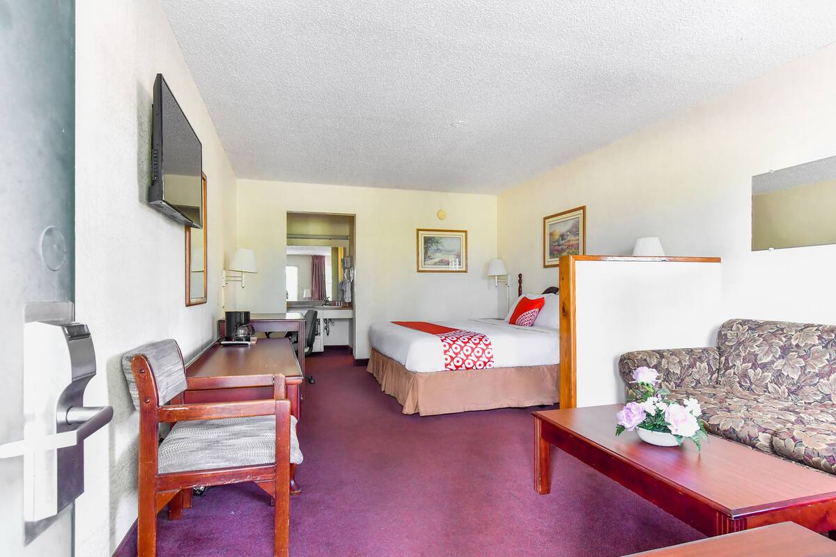 Ein Hotelzimmer mit einem Bett, einem Schreibtisch, einem Sessel, einer Couch und einem an der Wand befestigten Fernseher.