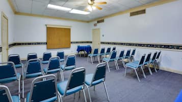 A conference room with rows of blue chairs, a ceiling fan, and a projector screen.