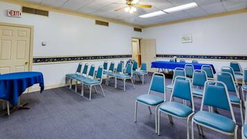 A conference room with rows of blue chairs, a blue table, and an exit sign.