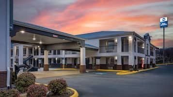 Two-story hotel with a flat roof and upper-level balconies, featuring a prominent entrance and parking area.
