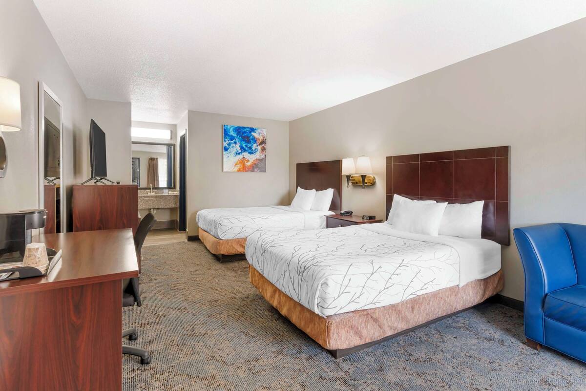 A hotel room with two beds, a desk, a chair, and a TV.