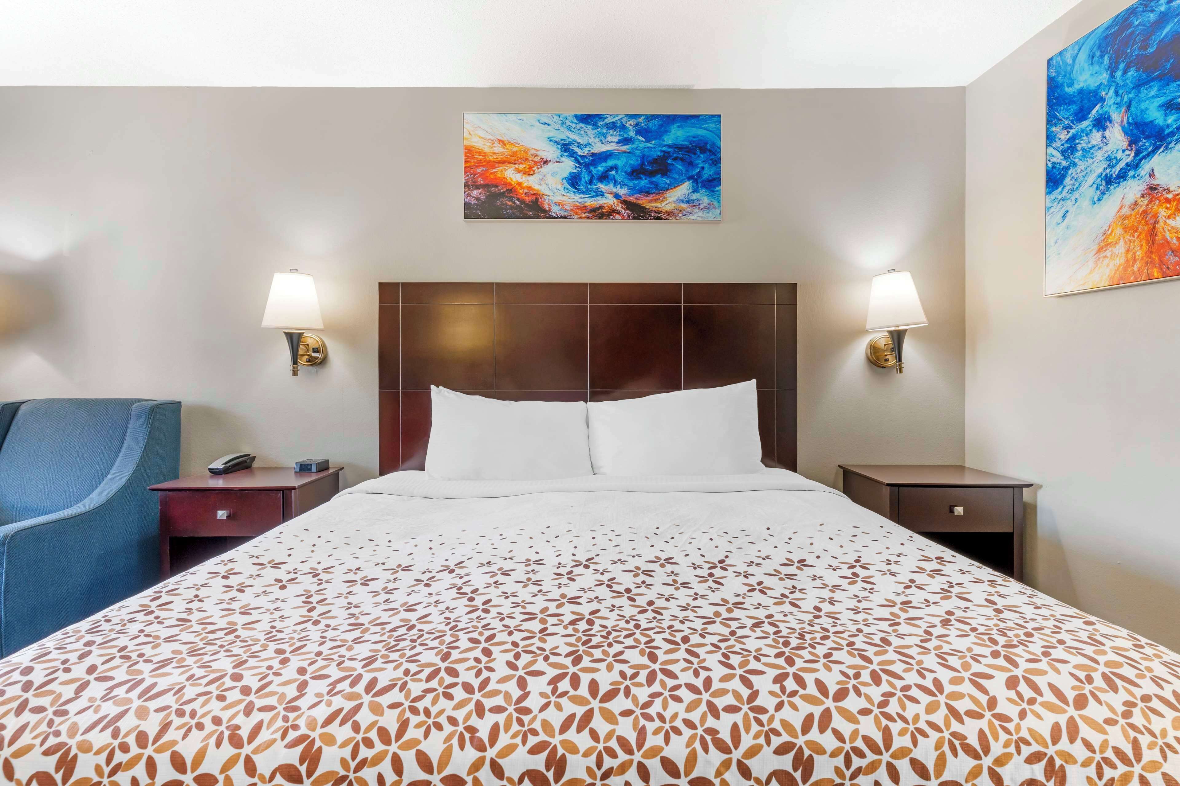 A hotel room with a large bed, two bedside tables, a chair, and two wall-mounted lamps.