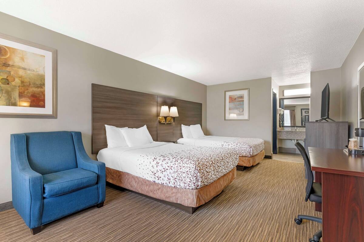 A hotel room with two beds, a blue armchair, a desk, and a TV.