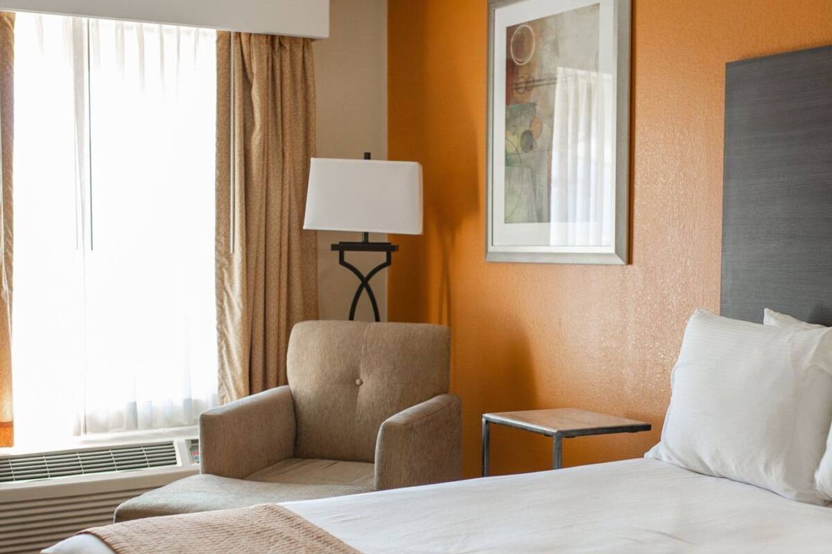 A hotel room with a large bed, a chair, a small table, and a window with curtains.