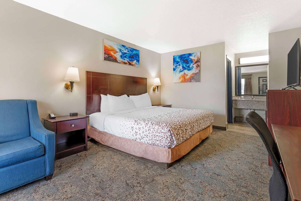 A hotel room with a bed, a desk, a chair, a nightstand, and artwork on the walls.