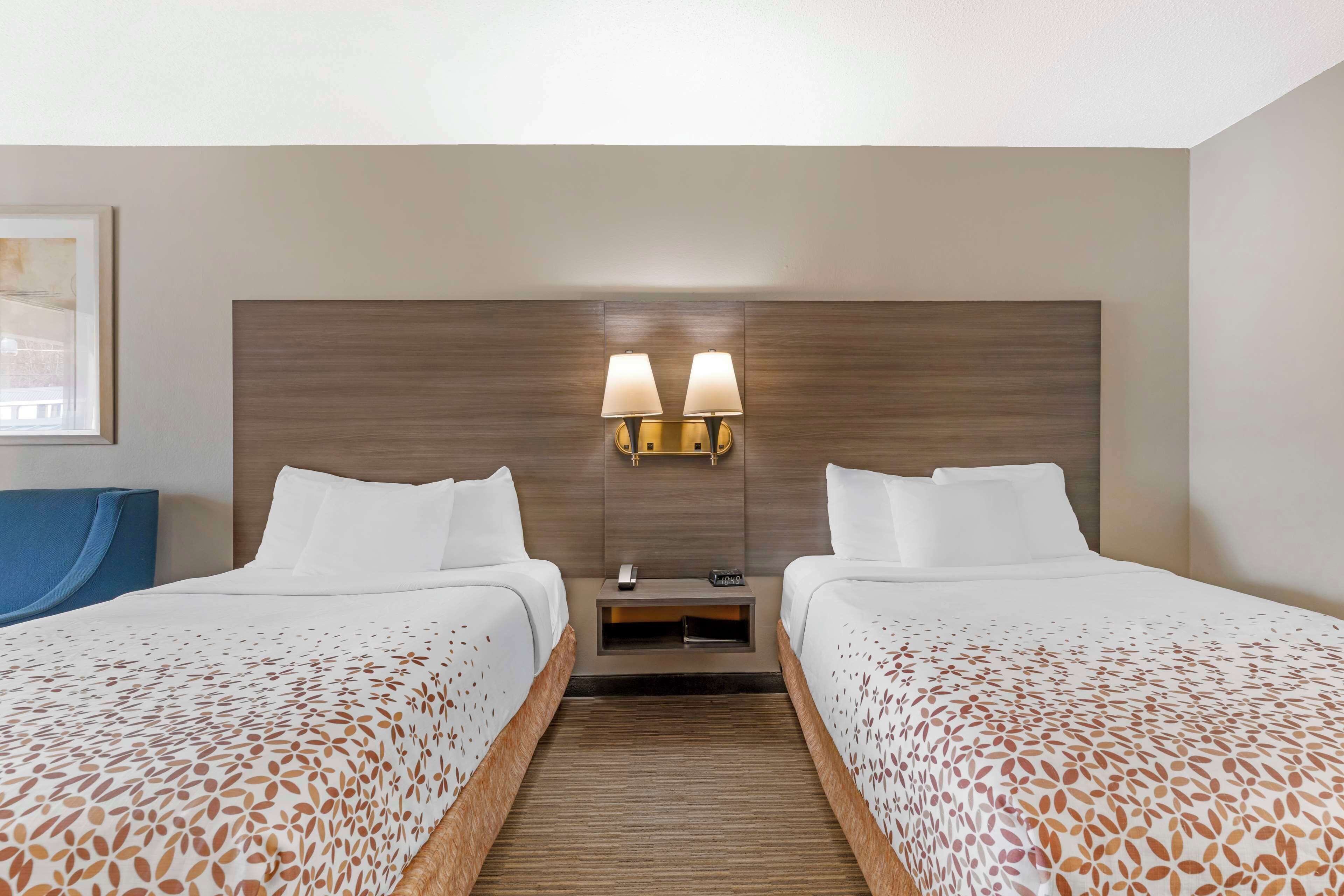 Une chambre d’hôtel avec deux lits, une tête de lit en bois, des tables de chevet avec des lampes et un tableau encadré au mur.