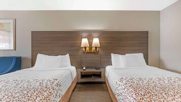 Une chambre d’hôtel avec deux lits, une tête de lit en bois, des tables de chevet avec des lampes et un tableau encadré au mur.