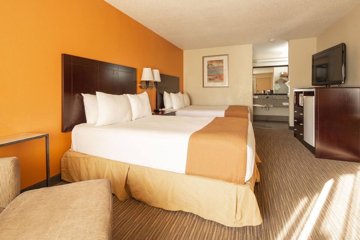 A hotel room with a large bed, a desk, a chair, a TV, and a bathroom visible in the background.