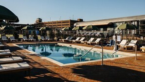 A pool area with lounge chairs and umbrellas, surrounded by a building with a flat roof and a parking garage in the background. - Best Western Royal Inn (Chattanooga)