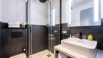 Une salle de bain moderne avec une douche à parois de verre, un lavabo blanc et un plan de toilette en marbre.
