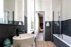 Un baño moderno con un lavamanos grande, una bañera y una ducha. Hay un tarro de vidrio en la encimera y una toalla colgada en la pared.