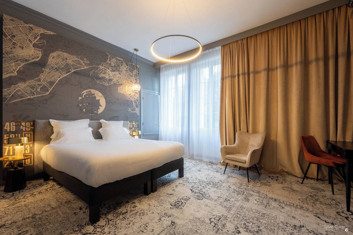 A modern hotel room with a large bed, a map mural, a round light fixture, a chair, and a table.