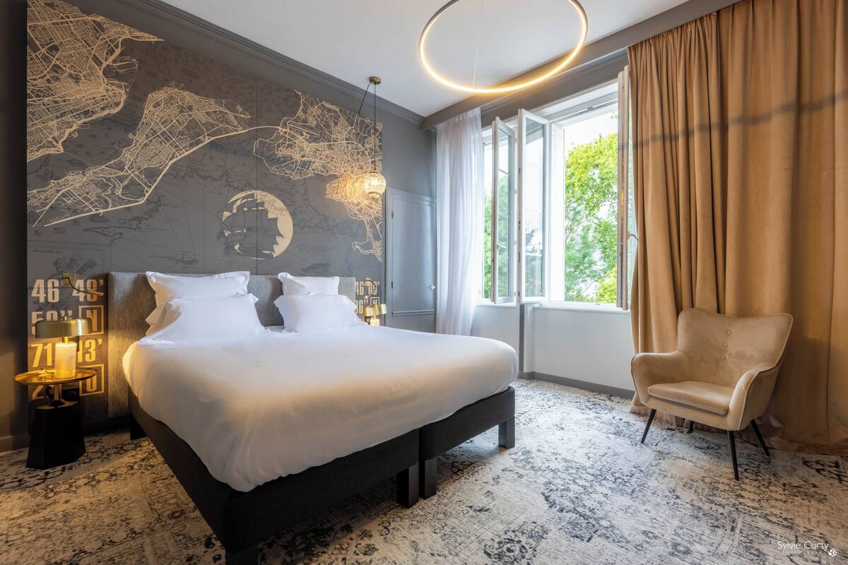 A modern hotel room with a large bed, a map on the wall, a chair, and a view of the outdoors.