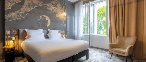 Een hotelkamer met een groot bed, een kaart aan de muur, een raam met gordijnen en een stoel.