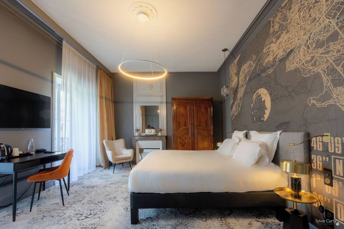 A hotel room with a bed, desk, chair, and a map on the wall.