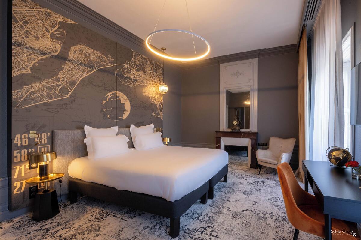 A modern hotel room with a large bed, a desk, and a chair. There is a map on the wall and a globe.