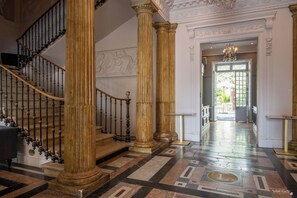 A grand staircase with ornate columns and a patterned floor, leading to a well-lit entrance.