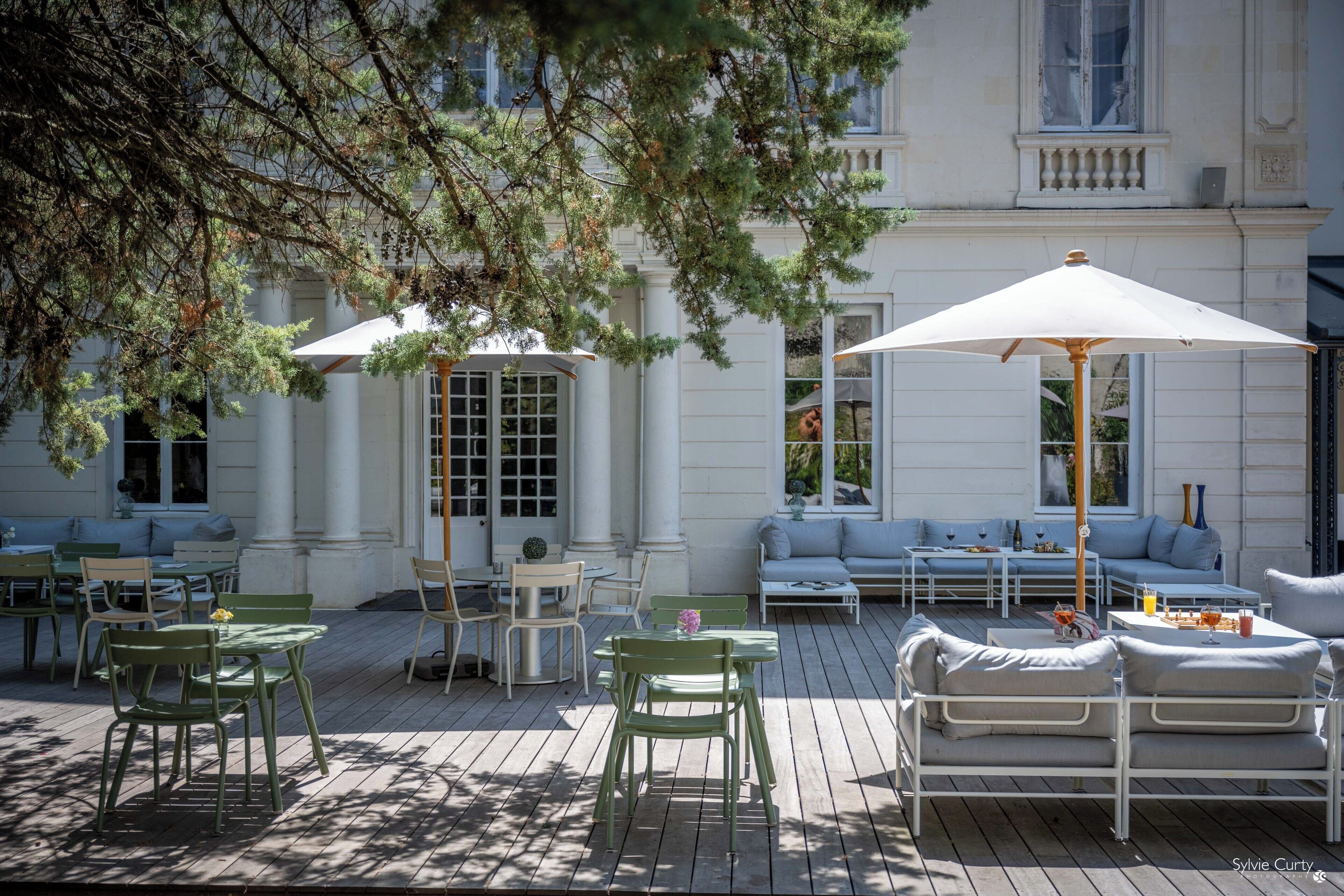 An outdoor patio with green chairs and tables, a white sofa, and umbrellas providing shade.