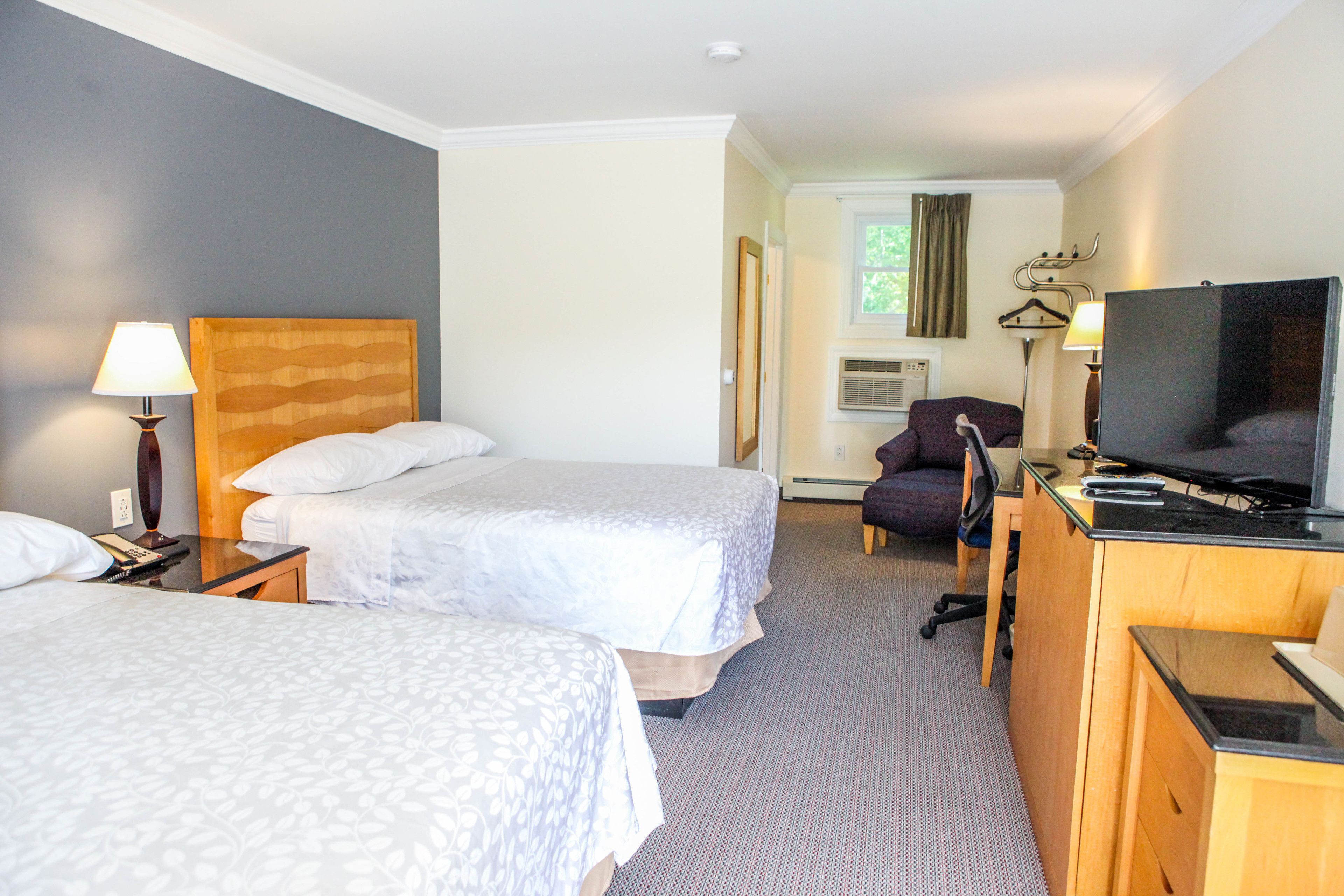 Quarto de hotel com duas camas, uma escrivaninha com televisão, uma cadeira e um abajur.