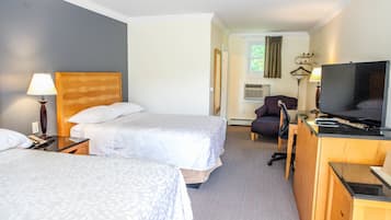 Quarto de hotel com duas camas, uma escrivaninha com televisão, uma cadeira e um abajur.