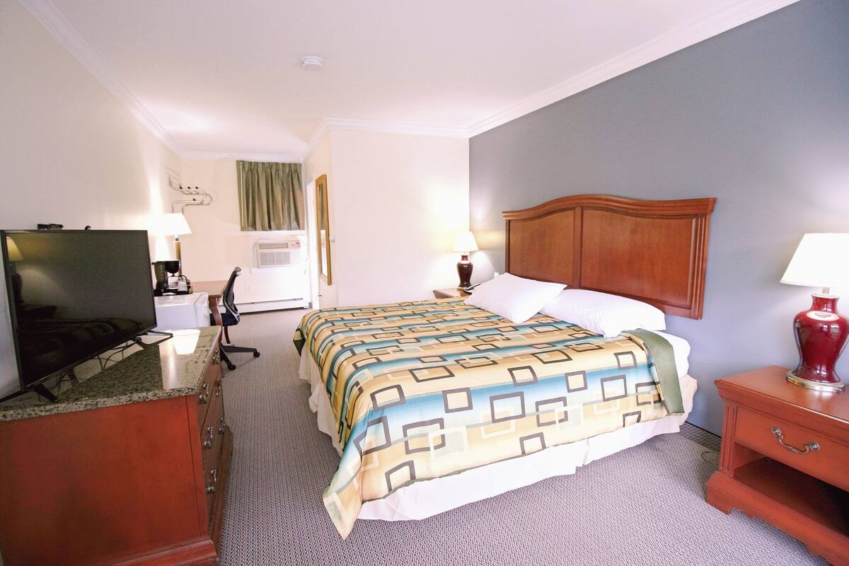 A hotel room with a bed, a desk with a television, a lamp, and a nightstand.