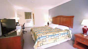 A hotel room with a bed, a desk with a television, a lamp, and a nightstand.
